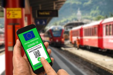 Tren istasyonundaki adam elinde Covid-19 için Avrupa Birliği dijital yeşil geçiş kartı olan akıllı telefon tutuyor. Coronavirus ve Yeşil Geçiş sırasında güvenli seyahat konsepti