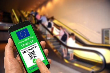 Alışveriş merkezinde elinde Covid-19 için Avrupa Birliği dijital yeşil kartı olan bir akıllı telefon tutan bir adam. Coronavirus ve Yeşil Geçit için güvenlik kavramı