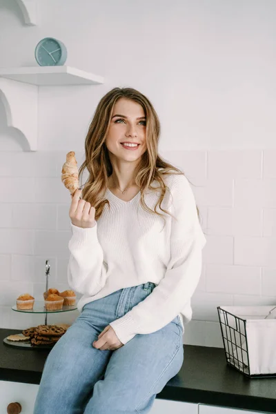 Hermosa chica rubia comiendo croissant por la mañana en la cocina — Foto de Stock