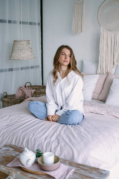 Hermosa chica rubia sentada en la cama en el dormitorio — Foto de Stock