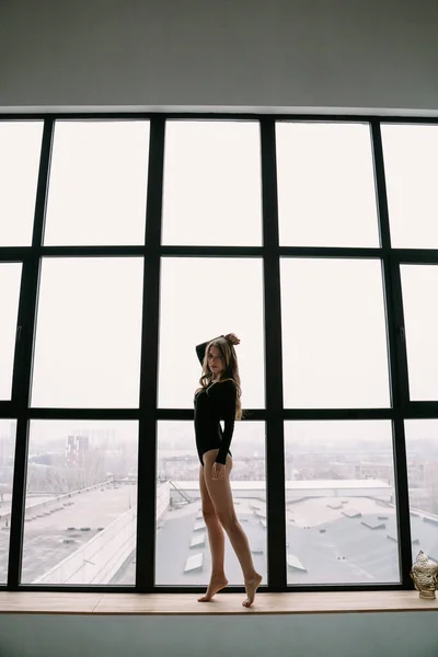Gyönyörű szőke lány, fekete ruhában, közel egy nagy ablakhoz. — Stock Fotó