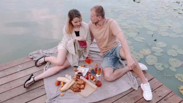 Petit ami et petite amie sont sur un pique-nique assis sur un quai en bois au bord du lac — Video
