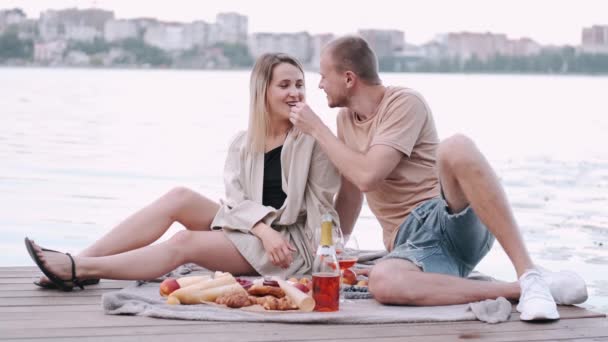 Парень и девушка на пикнике, сидят на деревянной набережной у озера. — стоковое видео