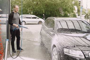 Siyah kazaklı bir adam arabasını yıkıyor.