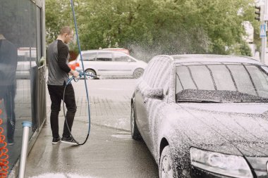 Siyah kazaklı bir adam arabasını yıkıyor.