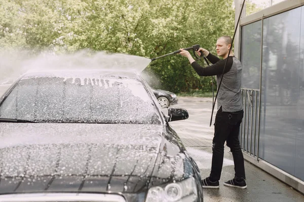 Siyah kazaklı bir adam arabasını yıkıyor. — Stok fotoğraf