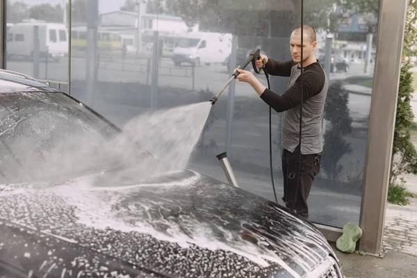 Homem bonito em uma camisola preta lavando seu carro — Fotografia de Stock