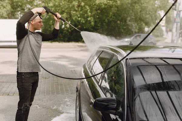 Homem bonito em uma camisola preta lavando seu carro — Fotografia de Stock