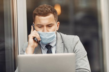 Maskeli bir iş adamı oturuyor ve bilgisayarı kullanıyor.