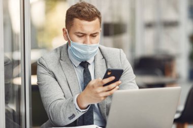 Maskeli bir iş adamı oturuyor ve bilgisayarı kullanıyor.