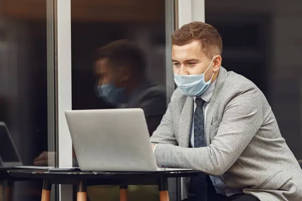 Empresario en una máscara sentado y utilizar el ordenador portátil — Foto de Stock