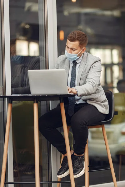 Empresario en una máscara sentado y utilizar el ordenador portátil — Foto de Stock