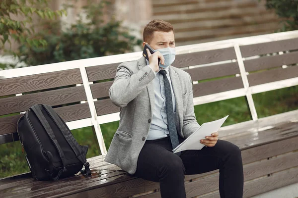 Empresario en una máscara sentado en un banco con documentos — Foto de Stock