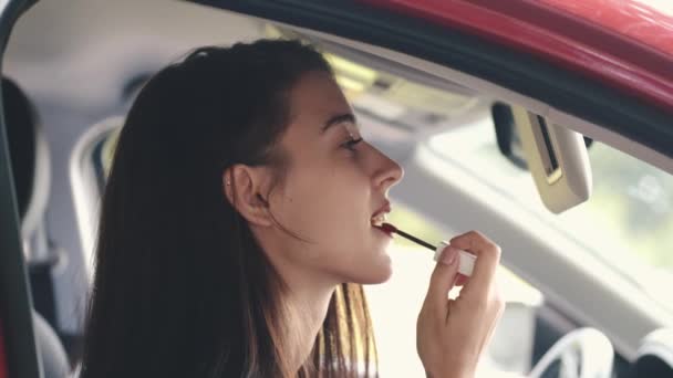 Jovencita pone en lápiz labial mirando en un espejo de coche — Vídeos de Stock