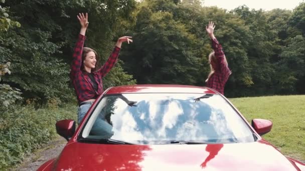 Red car with two girls from sides with hands up in nature — Stock Video