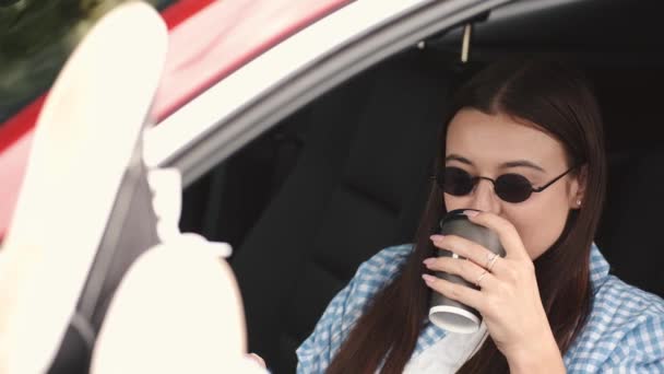 Girl in glasses sitting in a car ad drinking coffee to go — Stock Video