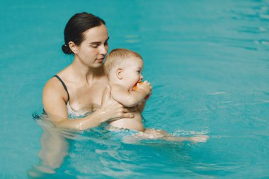 Anne ve küçük oğlu yüzme havuzunda yüzüyorlar.