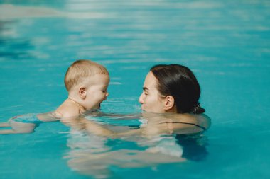 Anne ve küçük oğlu yüzme havuzunda yüzüyorlar.