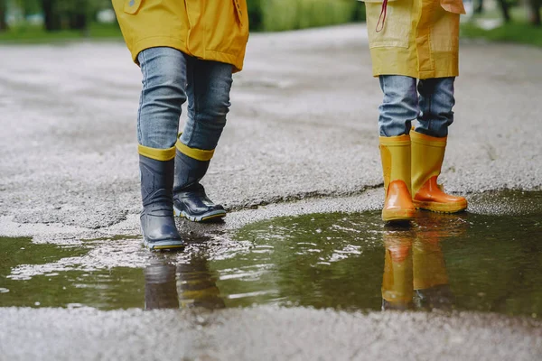 Çizmeli komik çocuklar su birikintisinin yanında kağıt gemiyle oynuyorlar.