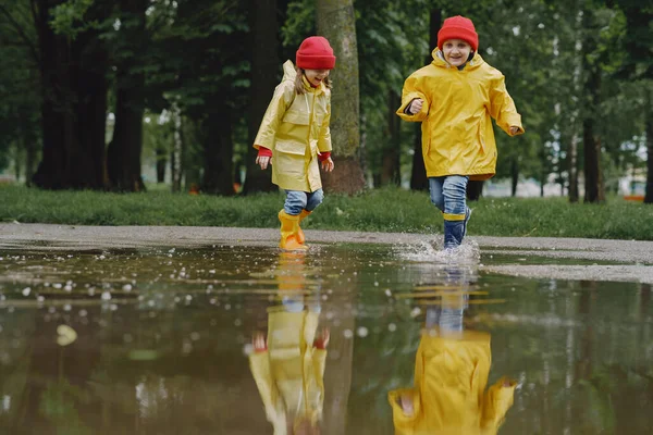 Funny kids in rain boots playing with paper ship by a puddle — Stock Photo, Image