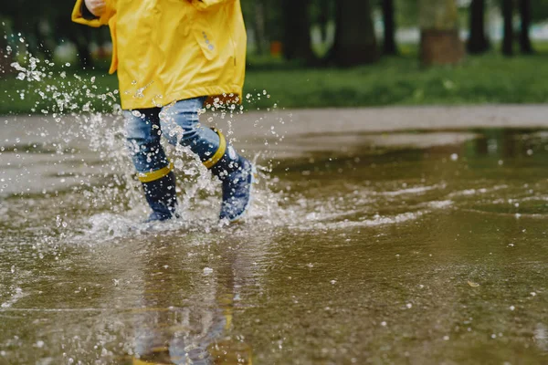 Çizmeli komik çocuklar su birikintisinin yanında kağıt gemiyle oynuyorlar.