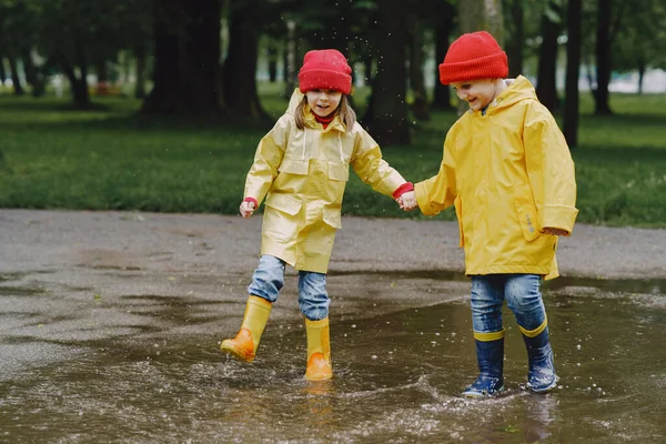 Funny kids in rain boots playing with paper ship by a puddle — Stock Photo, Image