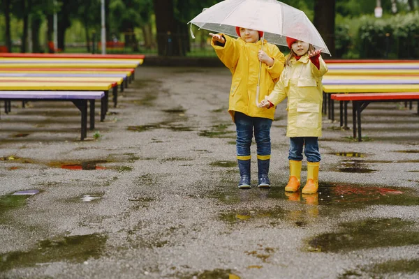 Vicces gyerekek esőcsizmában játszanak egy esős parkban. — Stock Fotó