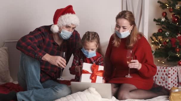 Feliz familia caucásica en máscaras sentados en casa decorada cerca del árbol brillante de Navidad en Nochevieja juntos — Vídeos de Stock