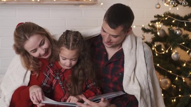 Genitori con figlia seduti a casa vicino all'albero di Natale e libro di lettura — Video Stock