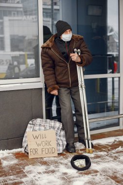 Kış şehrinde durgun elbiseli yaşlı evsiz bir adam.