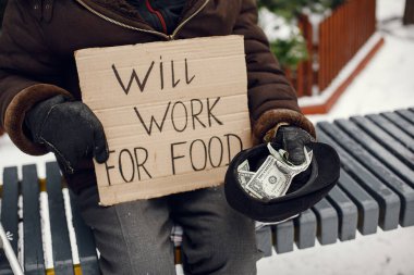 Kış şehrinde durgun elbiseli yaşlı evsiz bir adam.
