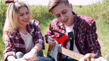 Erkek ve kadın bahar günü tarlada. Birbirine aşık çiftler bahar tarlasında vakit geçirir. Çimenler arka planda. Elektro gitarlı adam..