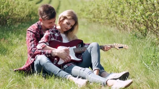 Muž a žena na poli na jaře. Pár zamilovaných tráví čas na jarním poli. Tráva na pozadí. Muž s elektro kytarou. — Stock video
