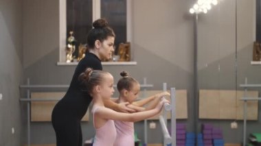 Genç öğretmen stüdyodaki dans sınıfında küçük balerinlere ders veriyor.