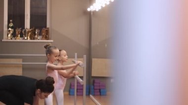 Genç öğretmen stüdyodaki dans sınıfında küçük balerinlere ders veriyor.