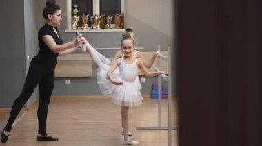 Genç öğretmen stüdyodaki dans sınıfında küçük balerinlere ders veriyor.