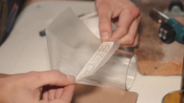 Adam atölyedeki el yapımı bir bardağa yapışkan etiket yapıştırıyor.