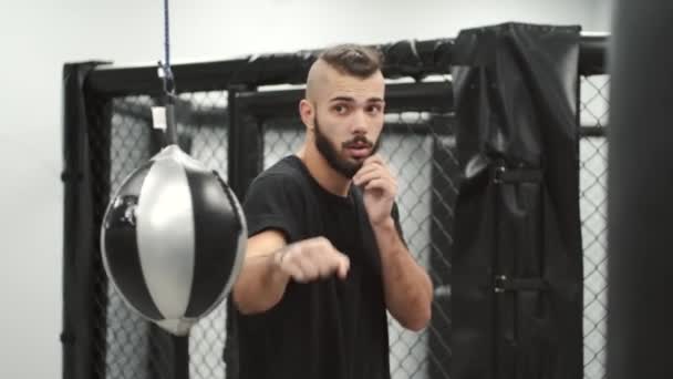 Barbudo hombre en ropa deportiva golpeando la bola de perforación en un gimnasio — Vídeo de stock