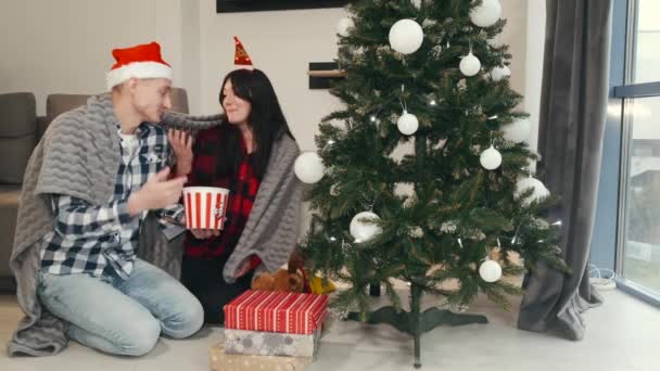 Молодая женщина и мужчина едят попкорн на рождественской елке — стоковое видео