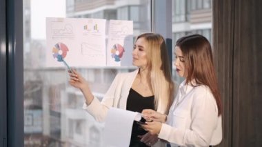 İki iş kadını ofis penceresinde bilgi grafiklerini tartışıyor