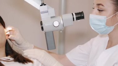 Klinikte genç bir kadının kulağını muayene eden bir doktor.