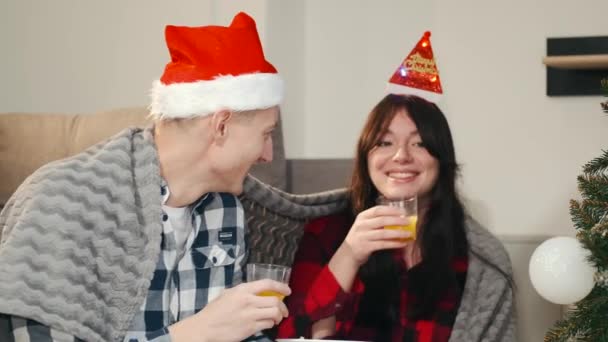 Casal feliz em santa chapéus beber suco perto da árvore de natal em casa — Vídeo de Stock