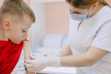 Kadın doktor izole edilmiş küçük çocuğa iğne yapıyor.