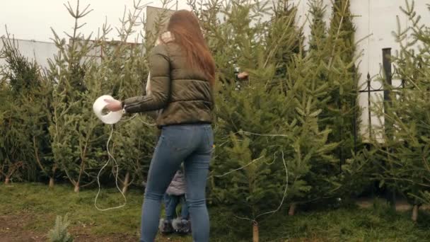 Rodina s malým dítětem balí vánoční strom s linií na venkovním trhu — Stock video