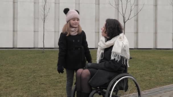 Kleine dochter wandelen met haar gehandicapte moeder in een stad — Stockvideo