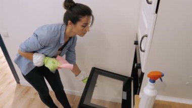 Genç bir kadın mutfakta fırın temizliyor.