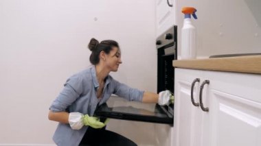 Genç bir kadın mutfakta fırın temizliyor.