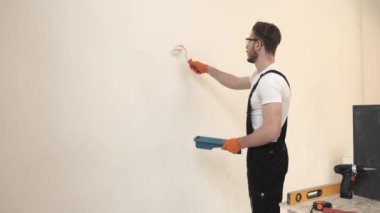 Siyah tulumlu boyacı beyaz duvarı silindir kullanarak boyuyor.
