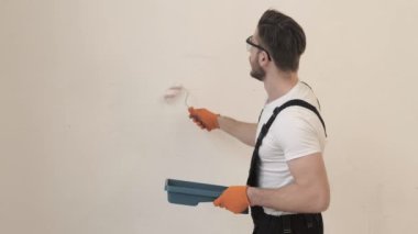 Siyah tulumlu boyacı beyaz duvarı silindir kullanarak boyuyor.