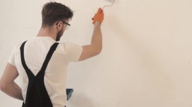 Siyah tulumlu boyacı beyaz duvarı silindir kullanarak boyuyor.
